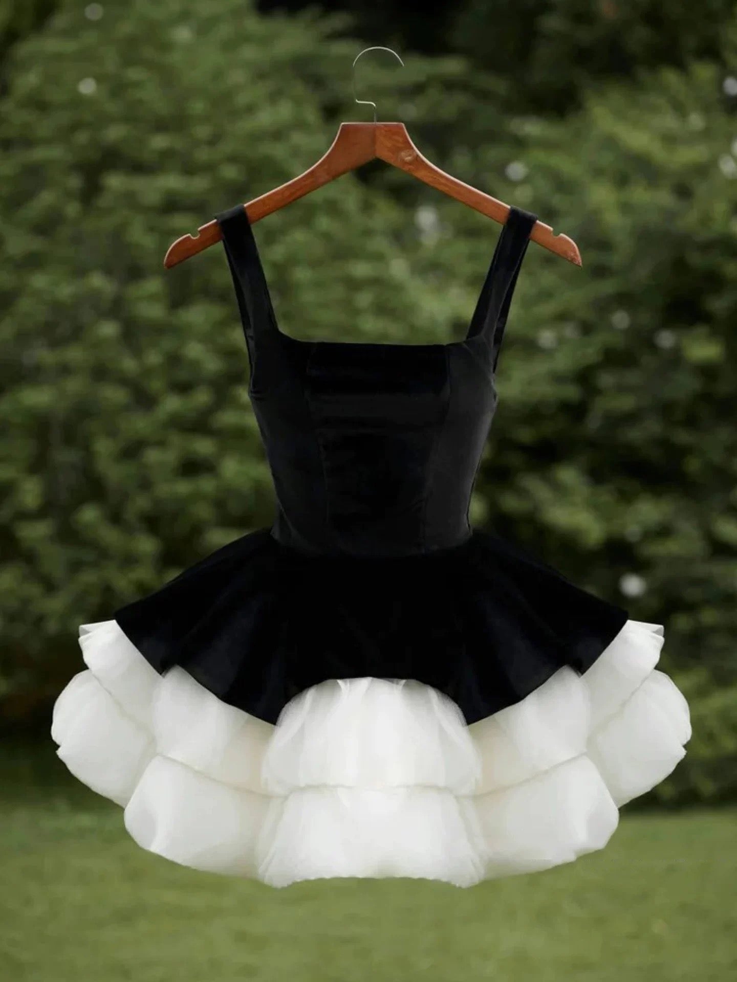 Black dress with white ruffled skirt on a hanger against a green background