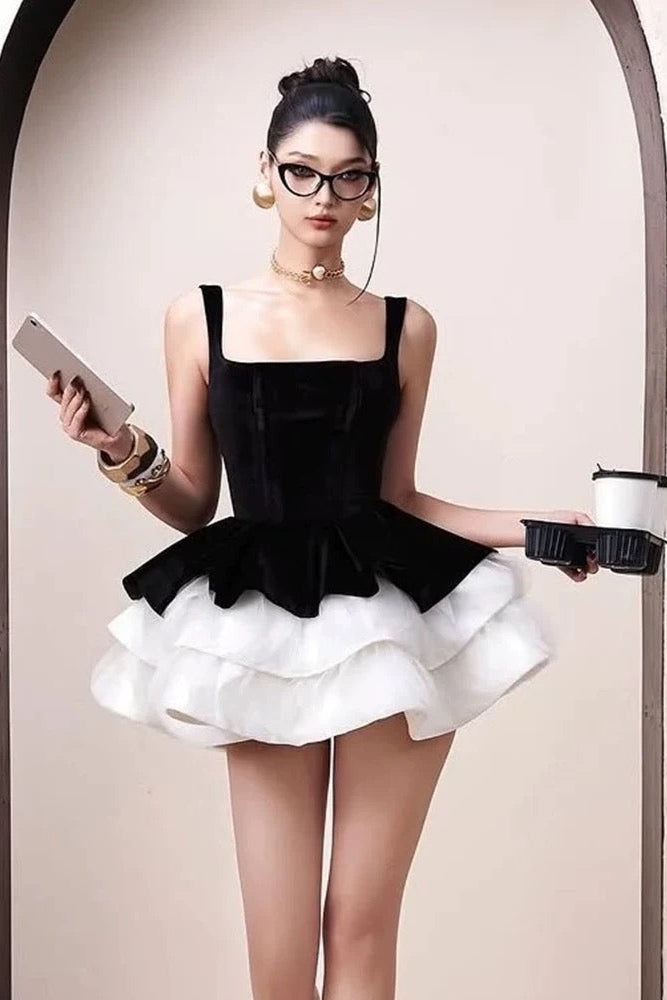 Woman wearing a black and white dress holding a phone and a cup.