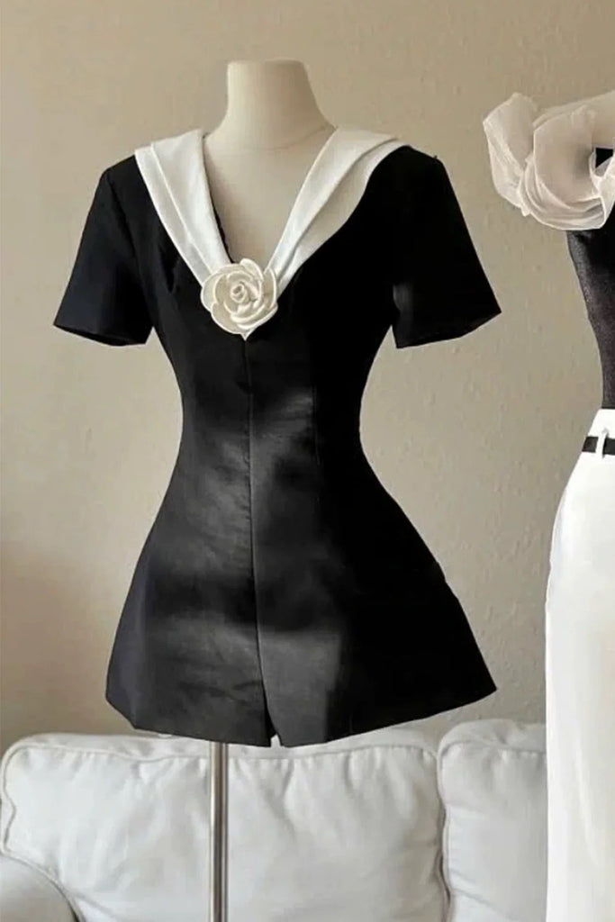 Black dress with white collar and rose detail on a mannequin against a beige wall.