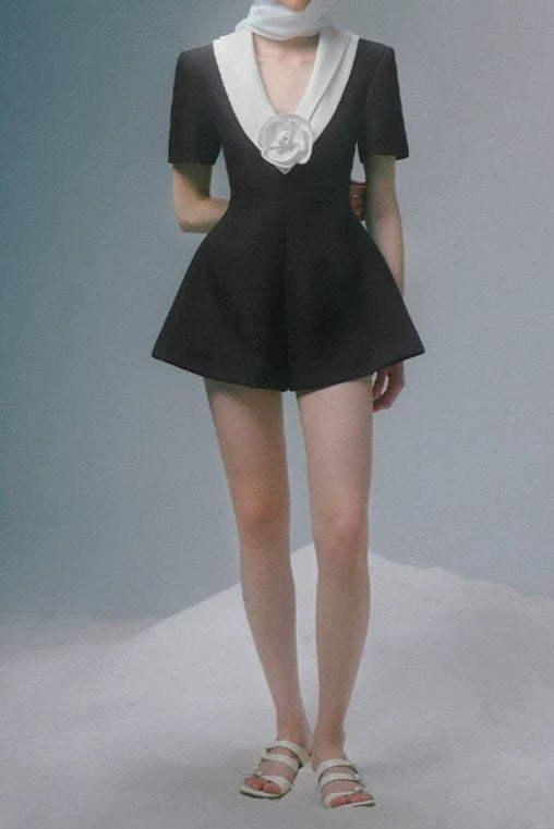 Woman wearing a black outfit with a white hat and scarf against a gray background